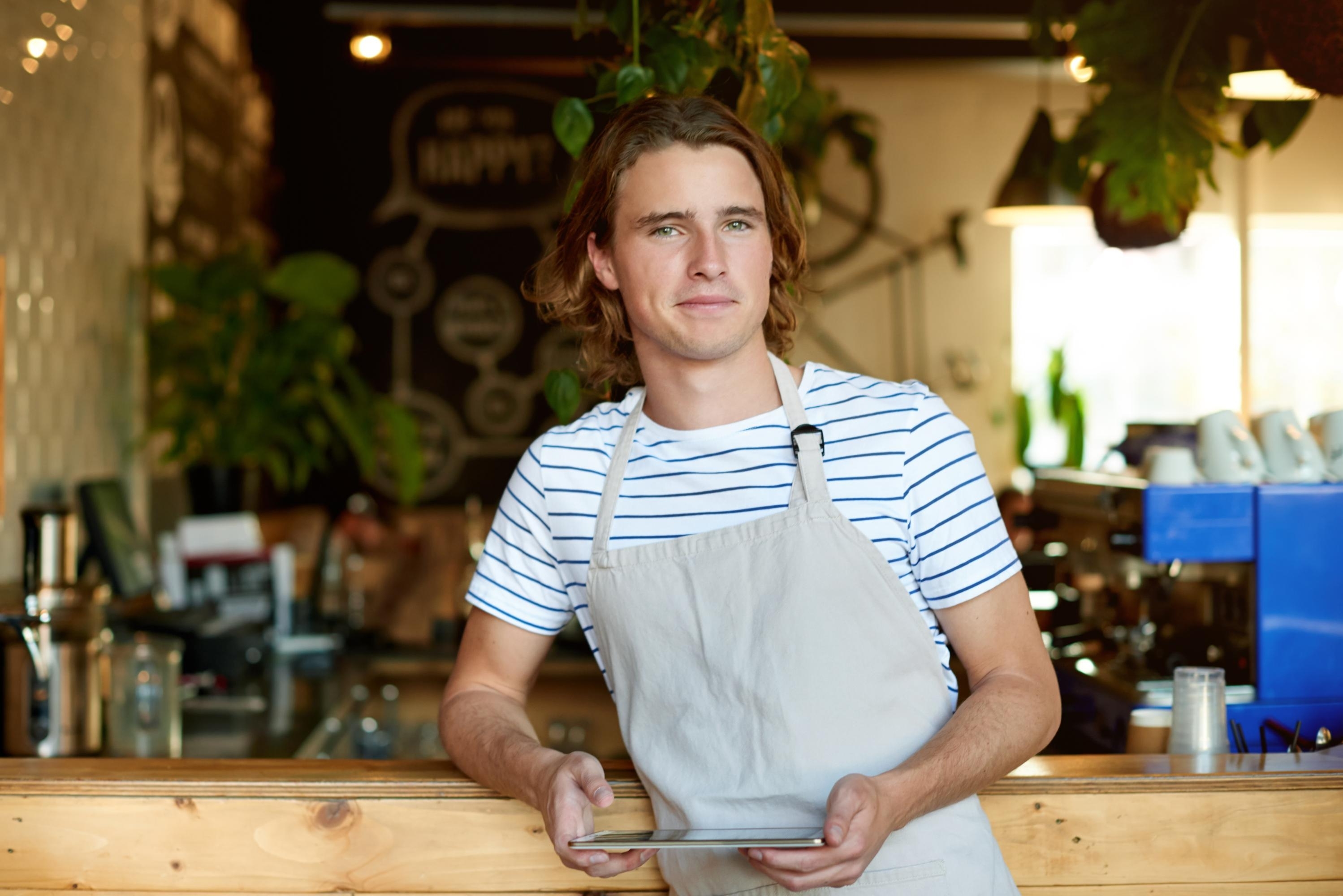 Ung man jobbar på ett café, står och håller i en surfplatta