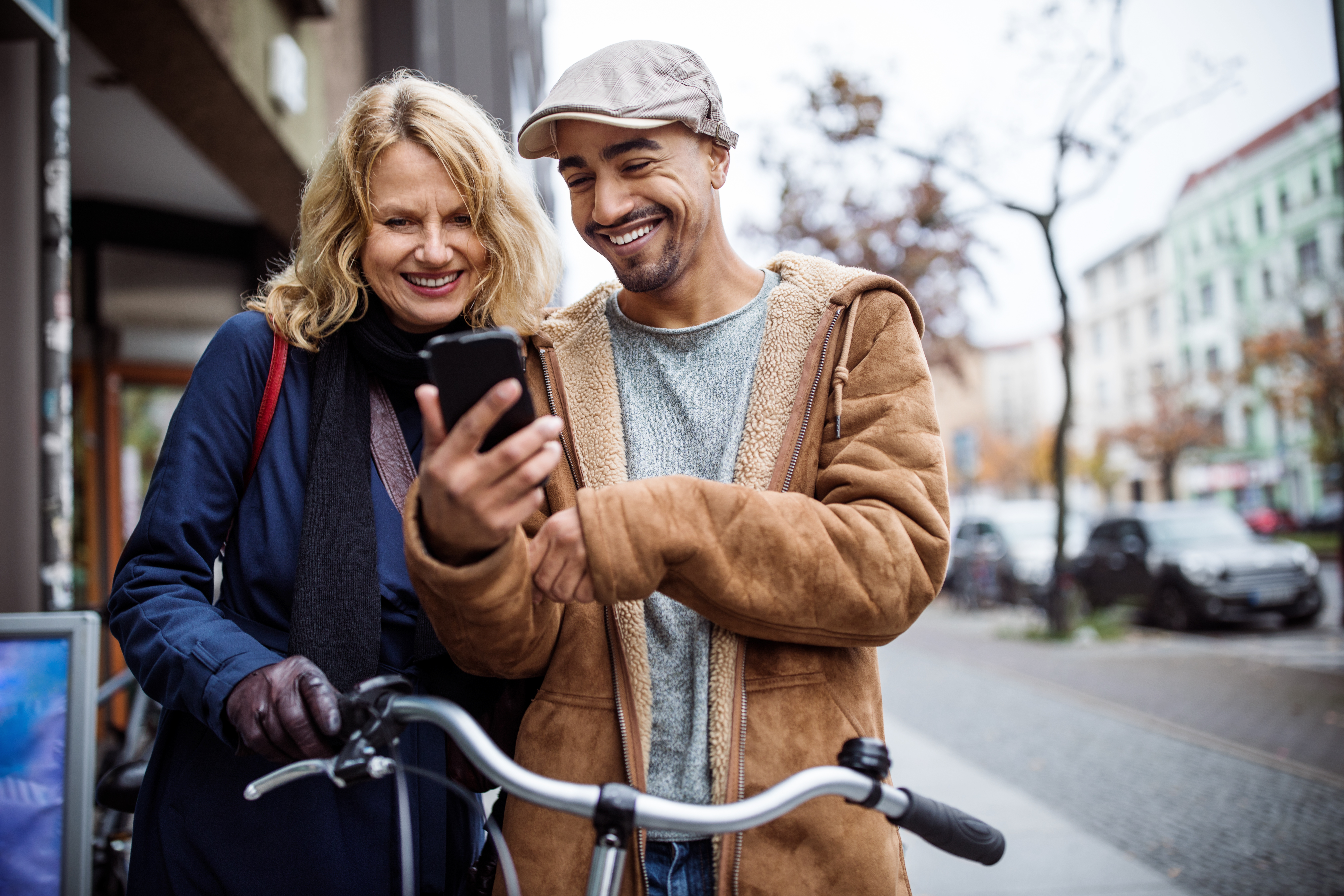 Leende man och kvinna står utomhus vid en cykel och tittar tillsammans på en mobiltelefon